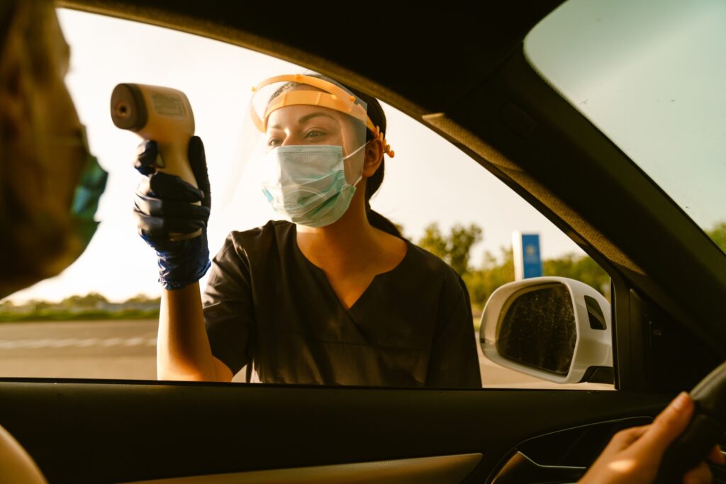 Black health worker measuring temperature of woman in car